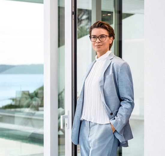 Frau mit Brille steht auf Terrasse und genießt den klaren Blick in die Ferne.